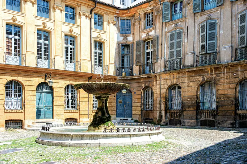 Place pavée d'Aix-en-Provence avec fontaine et façades aux volets bleus